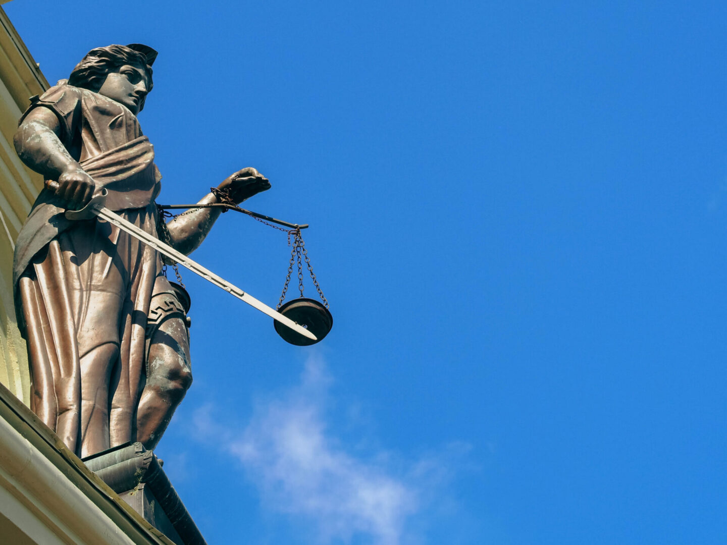 Statue of Lady Justice holding scales against a clear blue sky.