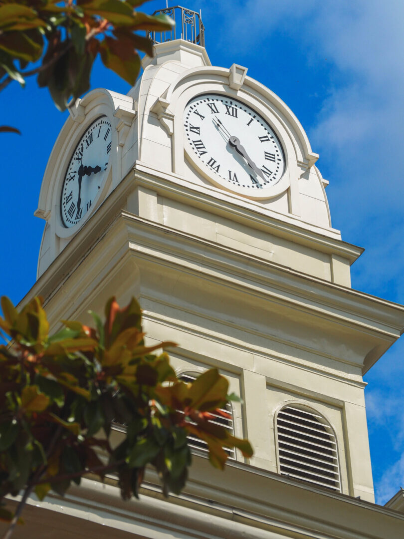 A close-up view of a white clock tower against a bright blue sky.